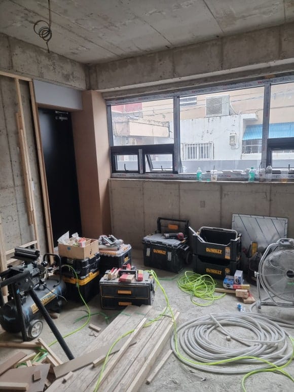 "전면 유리창 주변부의 목재 프레임 시공과 벽체 보강을 진행 중인 현장 모습으로, 우수한 마감 면 도출을 위해 다양한 정밀 공구들이 가지런히 정돈된 공정 전경"