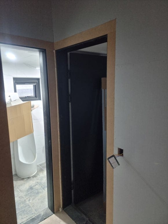 "투박한 철제 문틀 주변을 목재 판재로 빈틈없이 정밀하게 감싸 안아, 도장 및 필름 마감 후 군더더기 없는 미니멀 문선 라인이 연출되도록 시공한 모습"