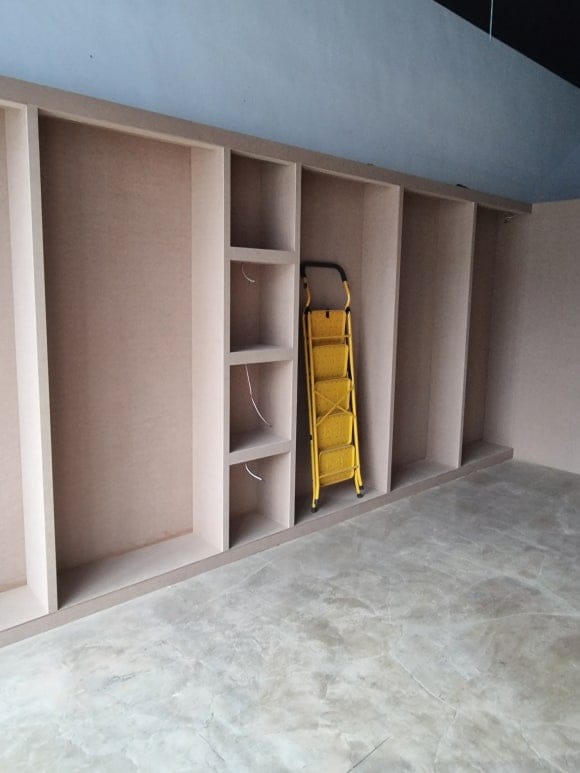 목작업 완료 후 마감 전 상태의 커튼 전시장으로, 폭이 다른 세로형 전시 칸과 중앙의 작은 선반 칸을 한 벽면에 함께 제작한 모습.