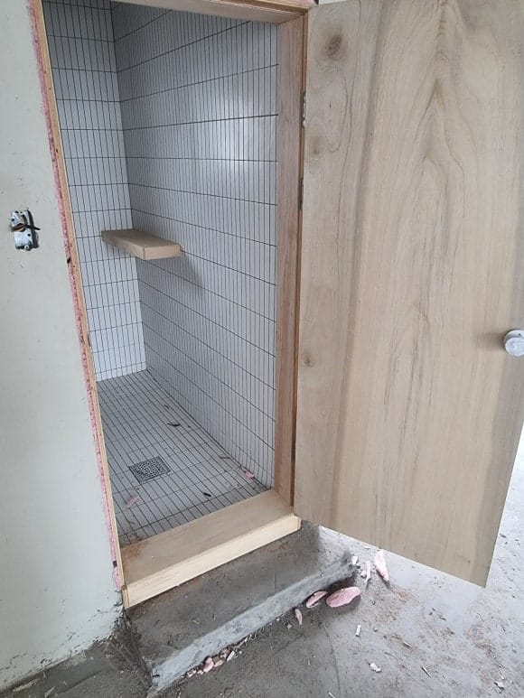 화장실 문을 연 상태로, 타일 마감된 내부 벽면과 우드크래프트가 제작한 작은 목재 선반이 보이는 모습.