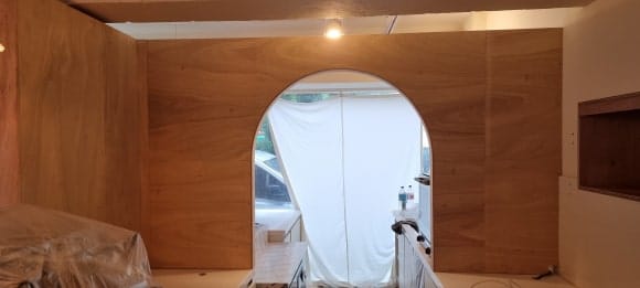 홀에서 주방 방향을 바라본 모습으로, 싱크대 상판 위에서 시작되는 아치형 게이트와 양옆 합판 벽체가 목공 상태로 완성됨.