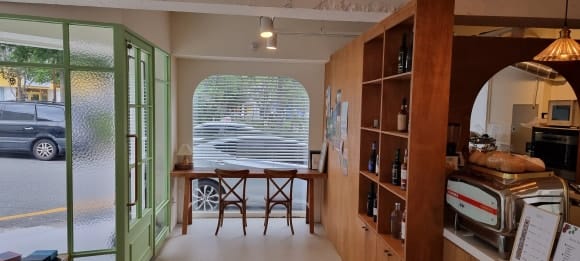 카페 홀 정면에서 통창 앞 아치형 게이트와 목재 파티션, 주방 출입 아치와 벽걸이 상부장이 함께 보이는 완공 모습.