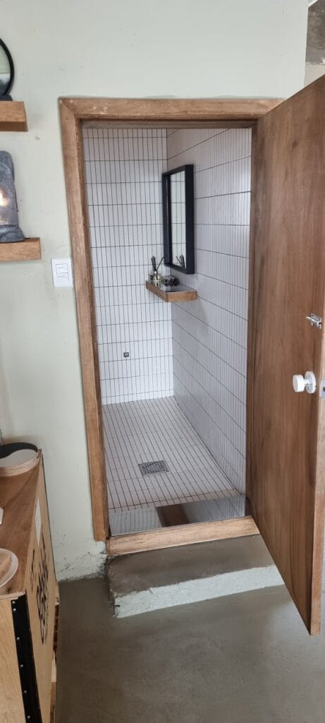 화장실 문을 열어 내부를 바라본 모습으로, 목재 문과 문틀 너머로 타일 마감된 화장실 공간이 연결되어 있습니다.