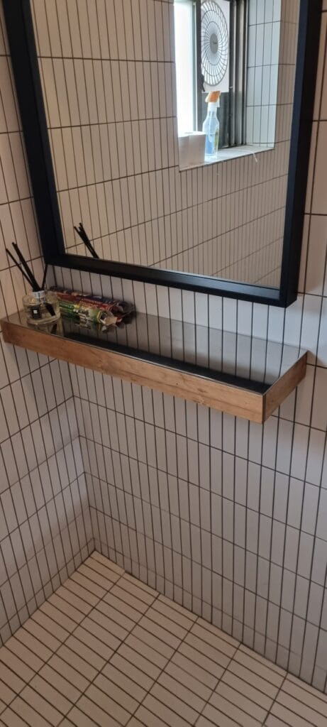 화장실 안쪽 벽면에 제작한 목재 선반 위로 스테인리스 판을 올려 마감하고, 거울 아래 수납 공간으로 사용 중인 모습.