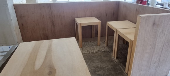 합판 주방 파티션 안쪽에 직접 제작한 소형 테이블들을 임시로 모아둔 모습으로, 각 테이블의 크기와 합판 옆면이 확인된다.