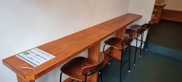 주방으로 이어지는 통로 벽면에 길게 제작한 목재 테이블을 측면에서 촬영한 모습으로, 여러 사람이 나란히 앉을 수 있는 구조입니다.