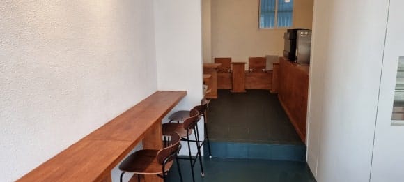 가게 입구에서 평상이 놓인 메인홀과 주방 공간을 연결하는 통로를 바라본 모습으로, 양쪽 벽을 따라 목재 가구가 배치되어 있습니다.