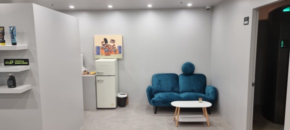 사진 10. 태닝샵 뒤쪽에 마련된 대기 공간으로, 중앙 탕비실 입구와 정수기, 우측 소파 및 태닝룸 출입문이 함께 보입니다.