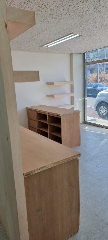 사진 19. 목공사 직후 매장 안쪽에서 바라본 모습으로, 카운터와 벽면 선반, 하부 수납장이 아직 오일스테인 마감 전의 목재 상태로 설치되어 있습니다.
