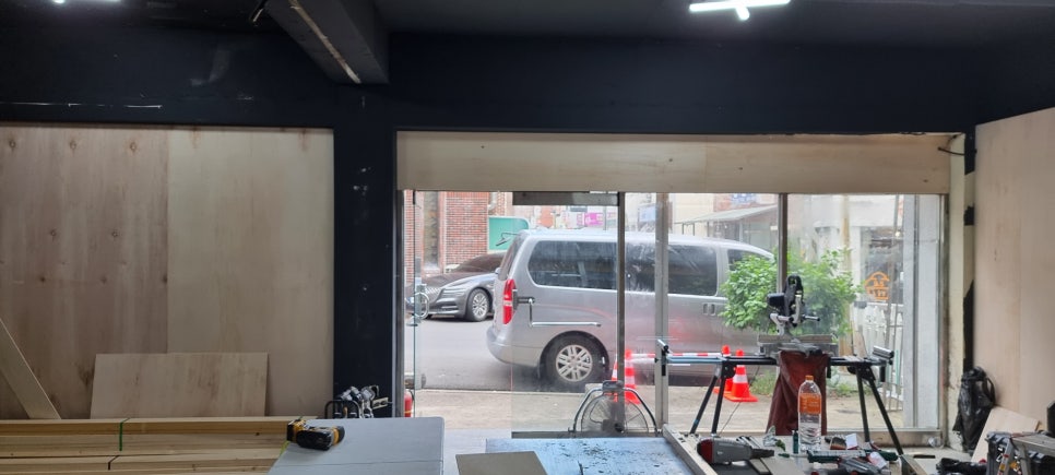 사진 33. 매장 안쪽에서 입구 방향을 바라본 모습으로, 입구 양쪽 벽면에 합판 작업이 진행되어 목재 면이 드러나 있습니다.